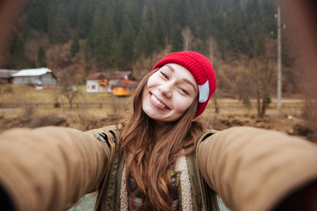 Picture of young cheerful woman standing on the bridge over the river and make a selfie.の写真素材
