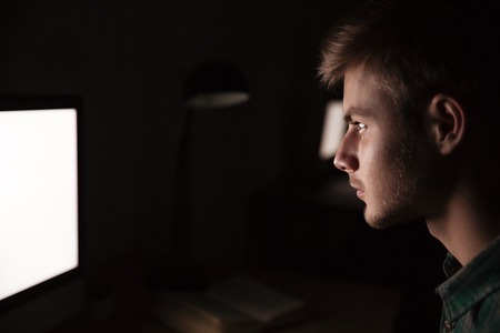 Serious young man using blank screen computer in the dark roomの写真素材