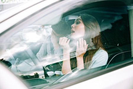 Side portrait of couple in car. woman paints her lips