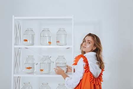 Attractive young woman taking jar with gold fish from the shelfの写真素材