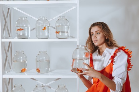 Cute young woman sitting and holding jar with gold fishの写真素材