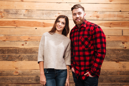 Happy casual couple standing together and looking at camera isolated on a wooden backgroundの写真素材