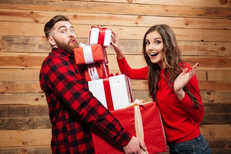 Cheerful happy couple standing with heap of xmas present boxes isolated on a wooden backgroundの写真素材