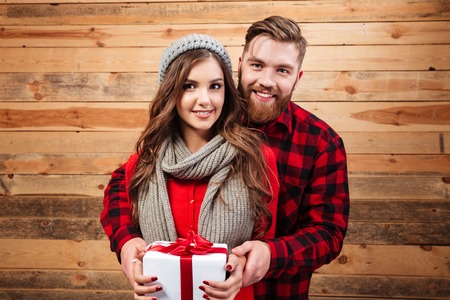 Models with gift. wooden background. girl in a cap and scarf. are looking at cameraの写真素材