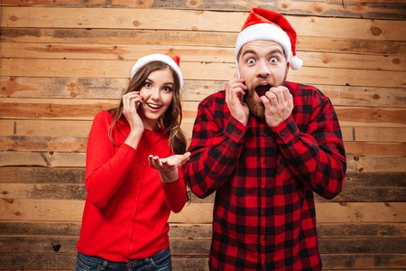Friends in santa's hats looking at camera. shocked. wooden backgroundの写真素材