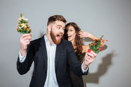 Attractive joyful couple in smart wear having christmas party over gray backgroundの写真素材