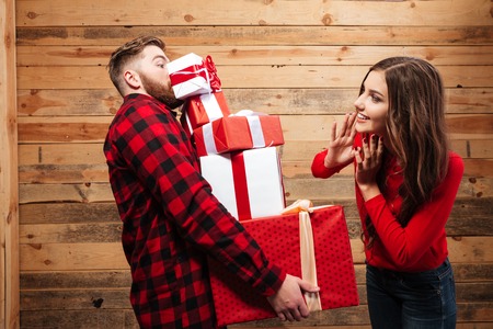 Young couple celebrating christmas with stack of heavy present boxes isolated on a wooden backgroundの写真素材