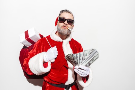 Modern man santa claus with gift sack smoking and holding moneyの写真素材