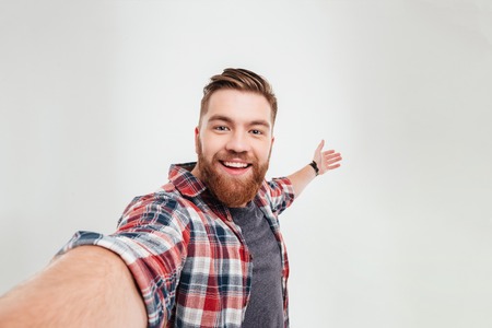Close up portrait of a cheerful bearded man taking selfie over white backgroundの写真素材