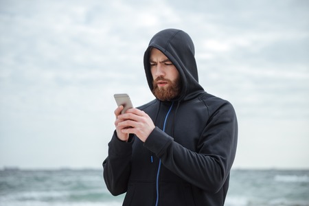 Runner with phone on beach. looking at phone