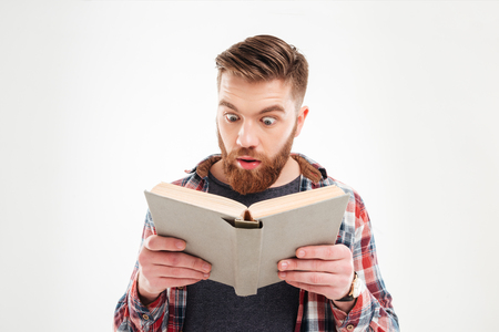 Young beraded man looking in book with eyes wide open over white backgroundの写真素材