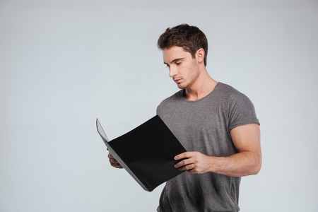 Portrait of a concentrated casual man holding folder over white backgroundの写真素材