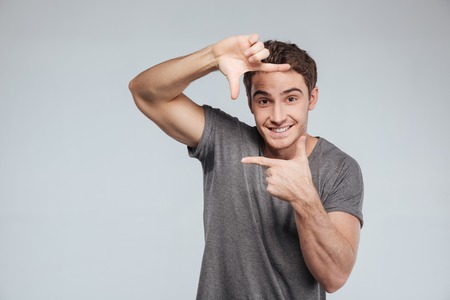 Portrait of a smiling casual man making frame with hands over white backgroundの写真素材