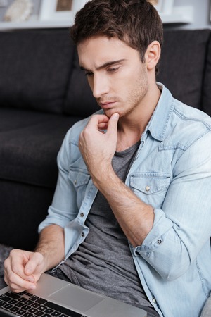 Close up portrait of a thoughtful young man working on laptop computerの写真素材