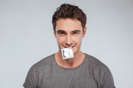 Close up portrait of a man holding condom in his mouth and looking at camera over white backgroundの写真素材