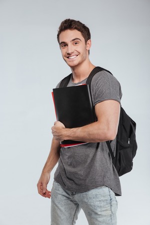 Portrait of a smiling male student with backpack and folders over white backgroundの写真素材
