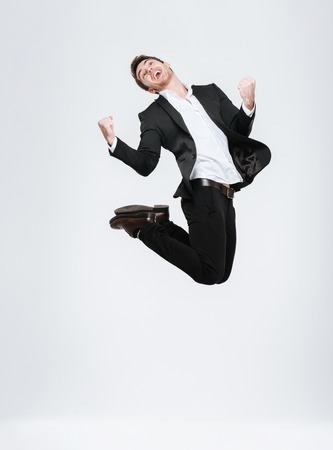 Full length happy business man in black suit jumping and celebrating success isolated on a white backgroundの写真素材