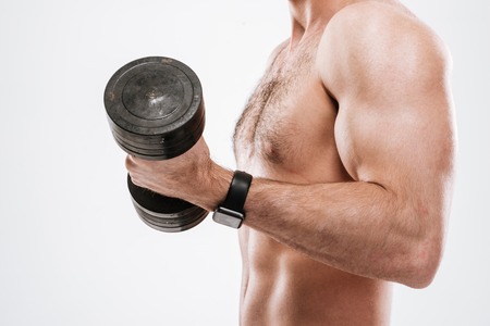 Cropped photo of handsome athlete standing with dumbbell in gym over white background.