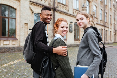 Group of cheerful friendly teenagers with books and backpacks walking together at university campusの写真素材