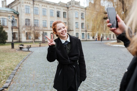 Smiling redhead woman student posing for a picture with university building on backgroundの写真素材
