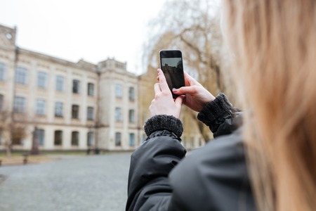 Back view of a young woman taking photo of a beautiful buildingの写真素材