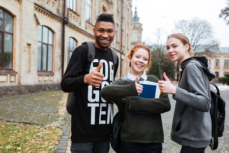 Portrait of a happy multiethnic students standing in university campus and showing thumbs upの写真素材