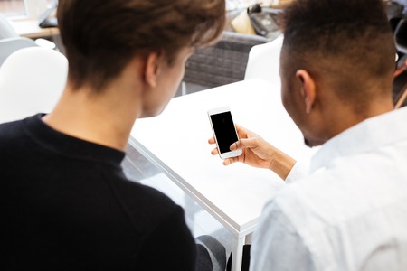 Back view image of two young students sitting in library and using cellphone. Looking at cellphone display.の写真素材