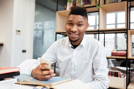 Picture of handsome african student in library learning education material with book while chatting...