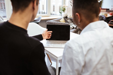 Back view photo of two young students sitting in library and using laptop computer.の写真素材