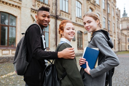 Group of young smiling students with books and backpacks walking together at university campusの写真素材