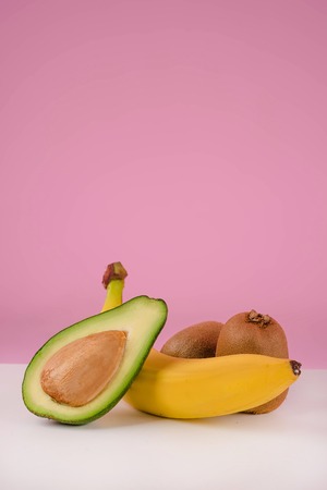 Fresh fruits on a table - sliced avocado, banana, kiwi isolated on pink backgroundの写真素材