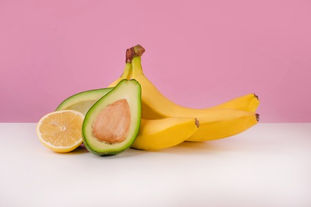 Fresh bananas, sliced avocado and lemon on table isolated on pink backgroundの写真素材