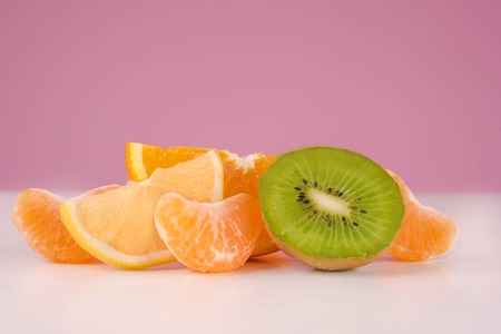Sliced fresh peeled kiwi, lemon, tangerine and orange on a table isolated on a pink background