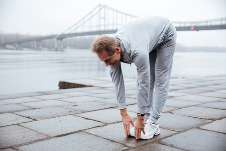 Full length Runner in gray sportswear warming up near the water. Side viewの写真素材