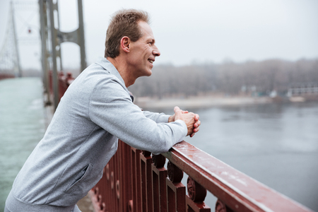 Side view of Smiling Runner in gray sportswear standing on bridge and looking awayの写真素材