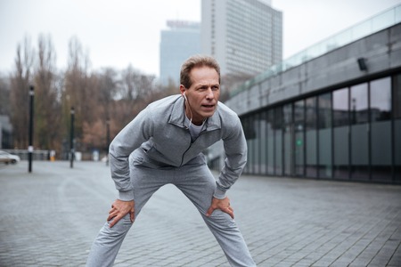Tired runner in gray sportswear standing and leaning on the street.の写真素材