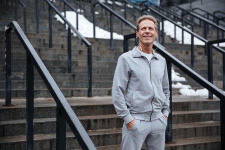 Runner in gray sportswear and headphone standing on stairs with arms in pocketsの写真素材