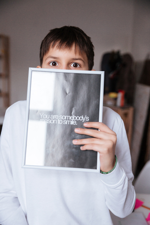 Cute little boy covered his face by poster with words You are somebody reason to smile