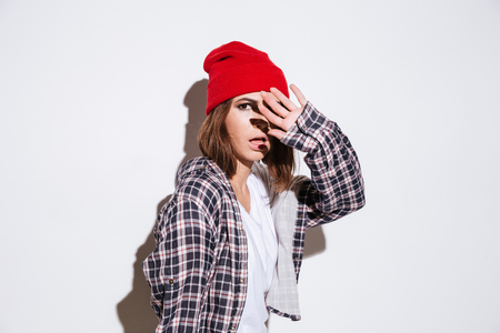 Picture of beautiful lady dressed in shirt in a cage print wearing hat standing isolated over white backgroundの写真素材