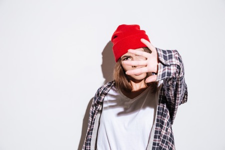 Young emotional lady dressed in shirt in a cage print wearing hat standing isolated over white backgroundの写真素材