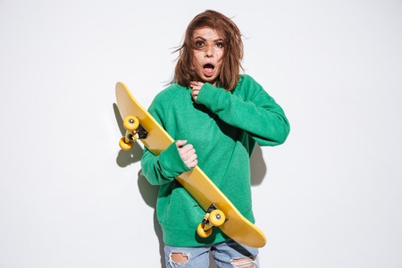 Picture of attractive skater lady dressed in green sweater standing isolated over white background with skateboard.の写真素材