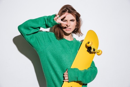 Photo of gorgeous skater lady dressed in green sweater standing isolated over white background with skateboard.の写真素材