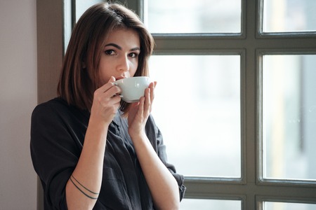 Image of young incredible cheerful woman look at camera in cafe and drinking coffee.の写真素材