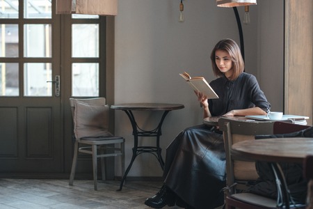 Image of beautiful young woman sitting at the table in cafe and reading book.