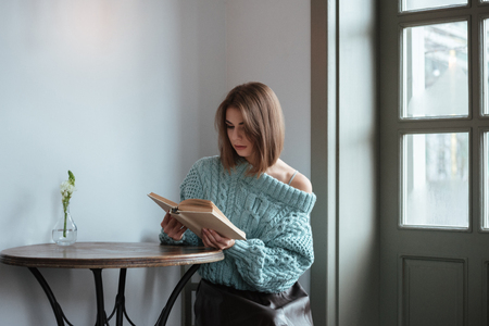 Image of pretty young lady sitting at the table in cafe and reading book.の写真素材