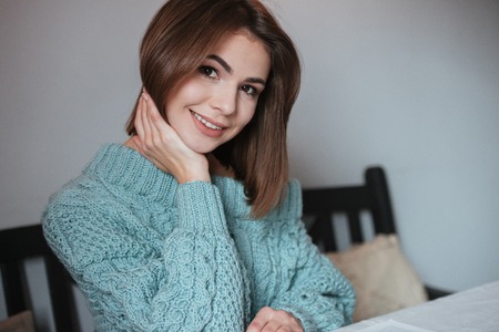 Picture of cheerful young lady sitting at the table in cafe and posing. Look at camera.