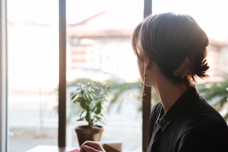 Back view image of young woman sitting at the table in cafe and looking aside.の写真素材