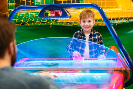 Smiling cute little boy playing air hockey with his father and having fun