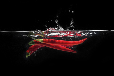 Red chili peppers falling into the water isolated on the black backgroundの写真素材