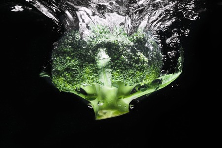 Fresh green broccoli dropped into water isolated on black backgroundの写真素材